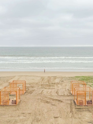 Ein Strand mit Holzkonstruktionen, eine Person geht spazieren und im Hintergrund das Meer.