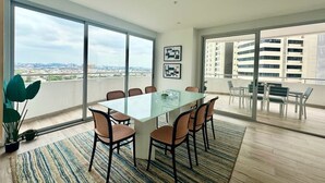 A modern dining area with a glass table and chairs, large windows, and a view of the city. - Luxurious Escape at Santana lofts includes Parking (Guayaquil)