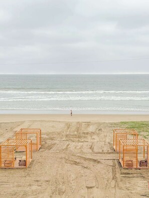 A beach with wooden structures, a person walking, and the ocean in the background. - Beachfront, pool, whirlpool & firepit (Montanita)