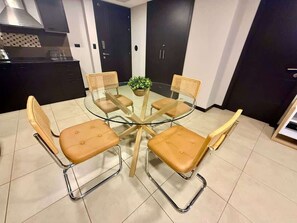 A dining area with a glass-top table surrounded by four chairs with metal frames and cushioned seats. - Stylish 2BD Condo with River View (Guayaquil)