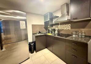 A modern kitchen with stainless steel appliances, a tiled backsplash, and dark cabinetry. - Stylish 2BD Condo with River View (Guayaquil)