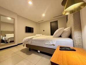 A hotel room with a bed, a large mirror, a flat-screen TV, and a wooden side table. - Stylish 2BD Condo with River View (Guayaquil)