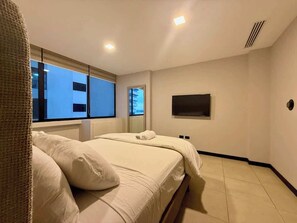 A bedroom with a bed, a window, a wall-mounted TV, and a door. - Stylish 2BD Condo with River View (Guayaquil)