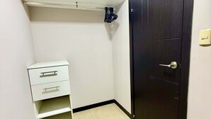 Una stanza piccola con una porta scura, uno scaffale bianco e un mobile contenitore con cassetti bianchi.