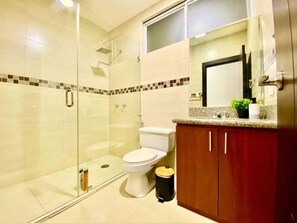 A bathroom with a glass shower enclosure, a toilet, and a wooden vanity with a mirror.