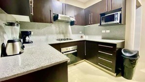 A compact kitchen with dark cabinetry, a microwave, a gas stove, and a coffee maker. - Poolside Condo w/Parking Near US Consulate (Guayaquil)