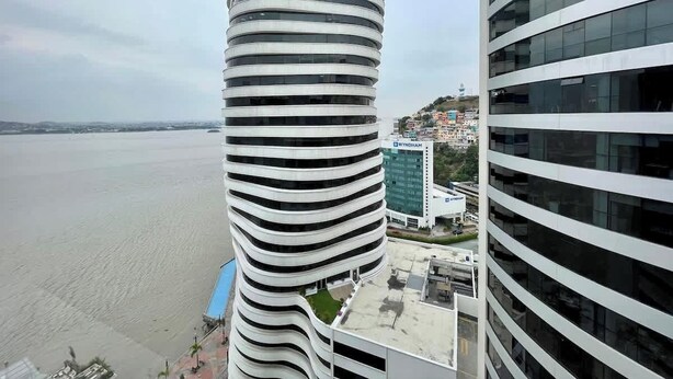Ein modernes Gebäude mit einem einzigartigen spiralförmigen Design, ein großer See im Hintergrund und Blick auf eine Stadtlandschaft.