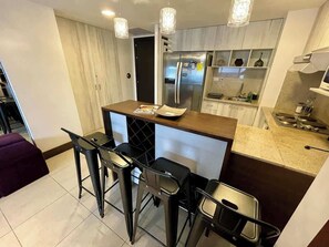 A compact kitchen with a central island, bar stools, a refrigerator, and a microwave. - Luxury Apartment on the 16th floor free Parking (Guayaquil)