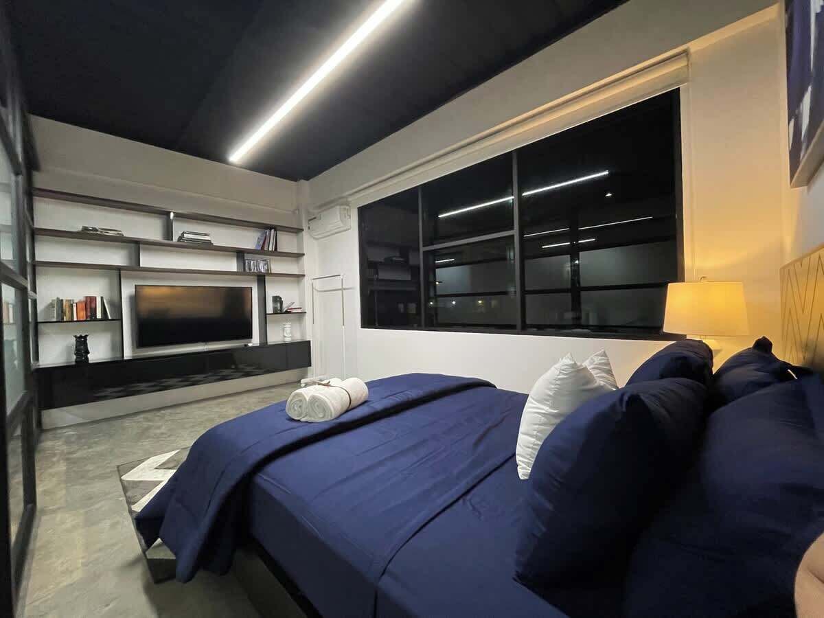 Ein modernes Schlafzimmer mit einem großen Bett, einem Flachbildfernseher, einem Fenster und einer eingebauten Bücherablage.