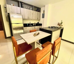 A compact kitchen with a refrigerator, stove, and cabinets. There is a dining table with chairs.