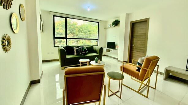 A modern living room with a sofa, two armchairs, a coffee table, and a TV.
