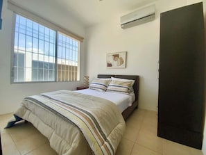Un dormitorio con cama, ventana, aire acondicionado y puerta.