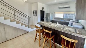 Una cocina moderna con una isla central, taburetes de bar, un refrigerador de acero inoxidable y una escalera.