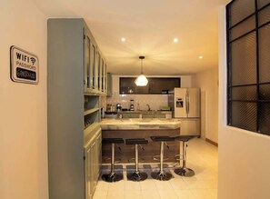 Une cuisine moderne avec un coin bar, un luminaire suspendu et un panneau indiquant le mot de passe du réseau Wi-Fi.
