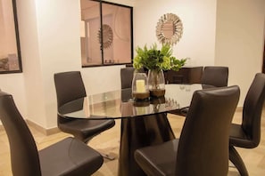 Un espace repas moderne avec une table en verre entourée de chaises en cuir, un miroir décoratif et une plante en pot.