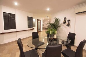 Un espace repas moderne avec une table en verre entourée de chaises, une plante en pot et des œuvres d’art décoratives accrochées au mur.