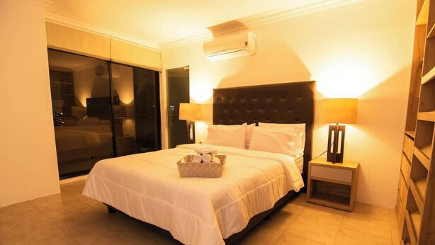 Habitación de hotel con una cama grande, una mesita de noche, una lámpara y un ventanal corredero que da a un balcón.