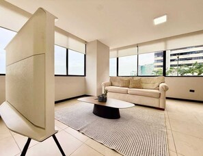 A modern living room with a sofa, coffee table, and a large window offering a city view. - Stylish 3BR Apartment with River View & Nightlife (Guayaquil)
