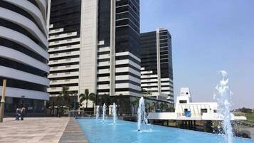 Un ensemble immobilier moderne comprenant un bâtiment principal, une fontaine centrale et une piscine.