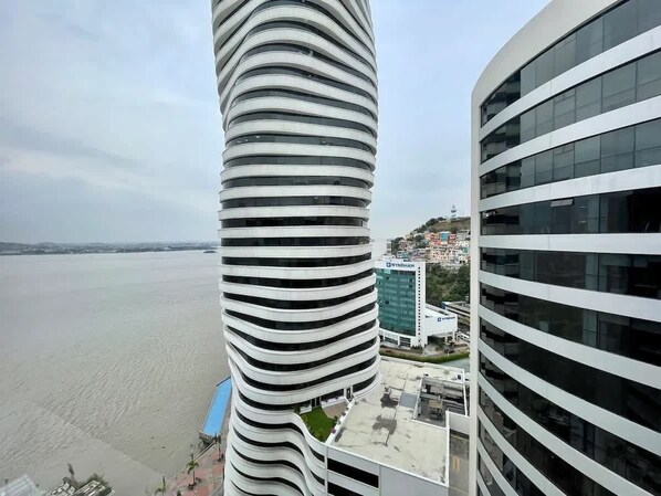 Ein modernes Gebäude mit einzigartigem spiralförmigem Design, Blick auf ein Gewässer und ein Nachbargebäude mit schlichter Fassade.