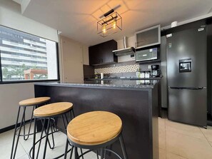 A modern kitchen with a central island, bar stools, a refrigerator, and a microwave. - Stylish 3BR Apartment with River View & Nightlife (Guayaquil)