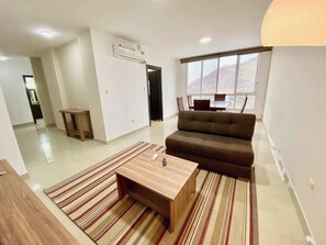 En moderne stue med sofa, sofabord og udsigt til bjerge gennem vinduet.