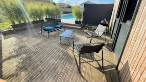 Een houten terras met buitenmeubilair, een zwembad en uitzicht op omliggende huizen.