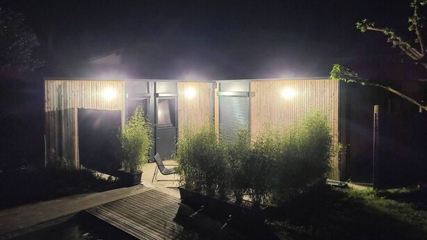 Een modern gebouw met een houten gevel, een overdekte ingang en een klein terras met een bank en plantenbakken.
