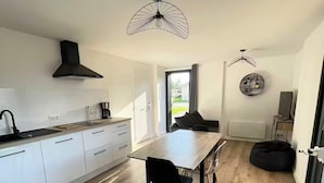 Een moderne keuken met witte kastjes, een zwarte afzuigkap, en een eethoek met een houten tafel en stoelen.