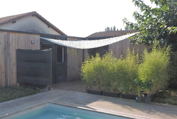 Un jardin avec une terrasse en bois, une piscine et un espace clos aménagé avec des plantes.