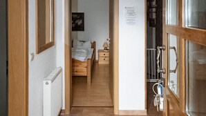 A narrow hallway leading to a bedroom with a bed, a nightstand, and a lamp. A radiator is visible on the left, and a door with a glass panel is on the right. - Gorgeous home in Röbel with lake view (Röbel)