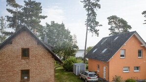 Ett bostadsområde med två hus, ett av tegel och ett orange, en bil parkerad framför det orange huset och ett litet förråd.