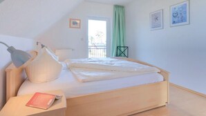 A bedroom with a bed, a desk with a lamp, a chair, and a window with a view.