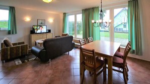 A dining area with a table and chairs, a sofa, a television, and a cabinet.