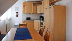 Eine kleine Küche mit Holzschränken, einem Esstisch mit Stühlen, einer blauen Tischläufer und einem schwarzen Toaster.