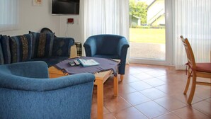 Ein Wohnzimmer mit einer Couch, einem Sessel und einem kleinen Tisch mit Fernbedienung und Buch.