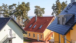 Ein Wohngebiet mit Häusern mit geneigten Dächern, einige mit Solaranlagen, und im Hintergrund freie Sicht auf das Meer.