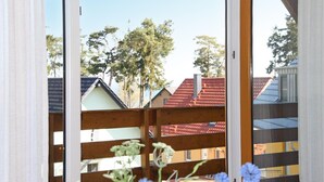 Blick durch ein Fenster auf einen Holzzaun, mit Häusern mit roten Dächern und einem Baum im Hintergrund.