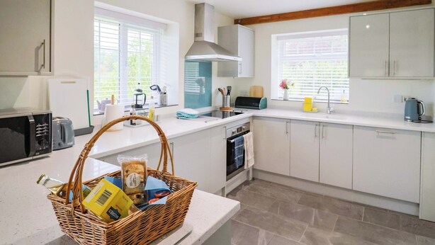 A modern kitchen with white cabinets, a built-in oven, and a large window providing natural light. - The Cottage Middle Westwater (Axminster)