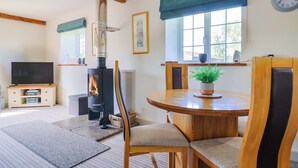 A cozy living room with a fireplace, wooden furniture, a television, and a dining area. - The Cottage Middle Westwater (Axminster)