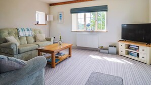 A living room with a sofa, a coffee table, a television, and a window with a view of greenery. - The Cottage Middle Westwater (Axminster)
