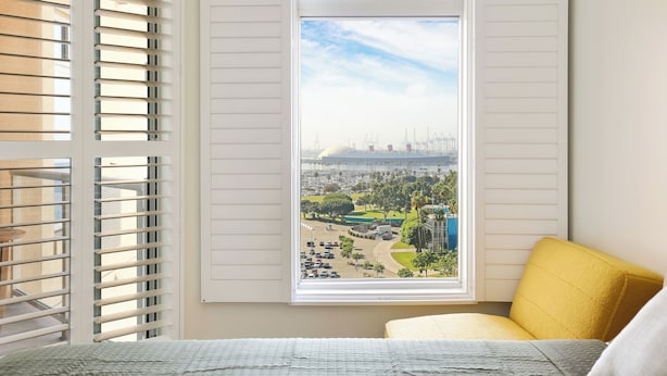Een kamer met een bed, een raam met zonwering en uitzicht op een stadsbeeld.