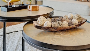 Een moderne woonkamer met een ronde salontafel, een geel fauteuil, een witte bank en decoratieve items, waaronder een houten dienblad met ballen.