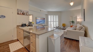 Een moderne keuken met een centraal eiland, een zithoek met een bank en tafel, en een woonkamer met een sofa en een plant.