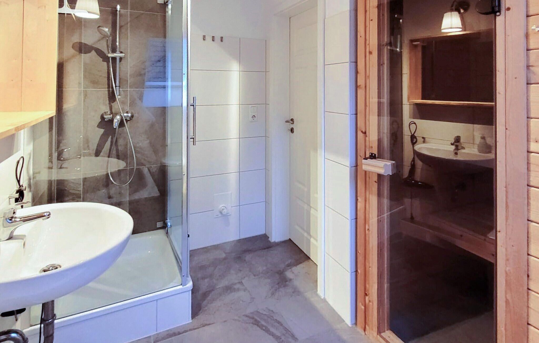 A bathroom with a glass shower enclosure, a white sink, and a wooden vanity with a mirror.