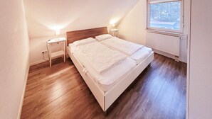 Ein Schlafzimmer mit einem Doppelbett, zwei Nachttischen, einem Heizkörper und einem Fenster mit Blick.