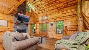 L’intérieur d’une cabane en rondins, avec une cheminée en pierre, des murs en bois et un coin salon confortable.