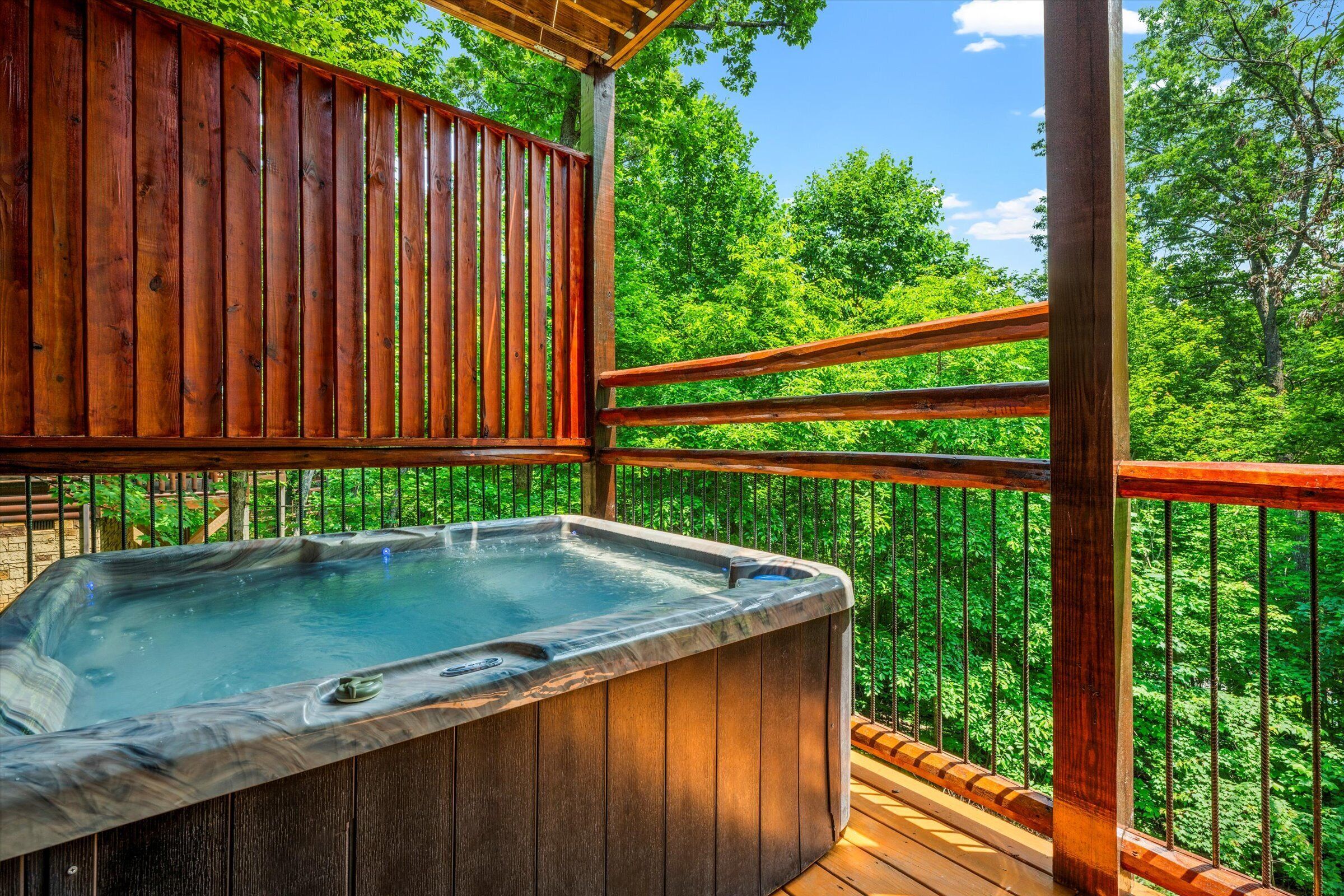 A hot tub on a wooden deck with a view of a forest.