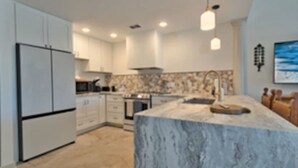 A modern kitchen with white cabinetry, a marble island, and pendant lighting. - One - Too - Suite, Saint George Island, Beach Townhome (Eastpoint)