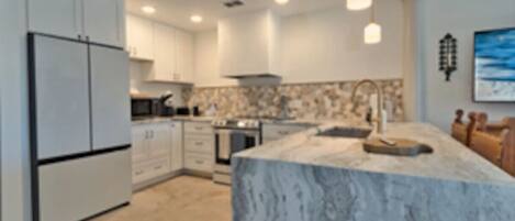 A modern kitchen with white cabinetry, a marble island, and pendant lighting.